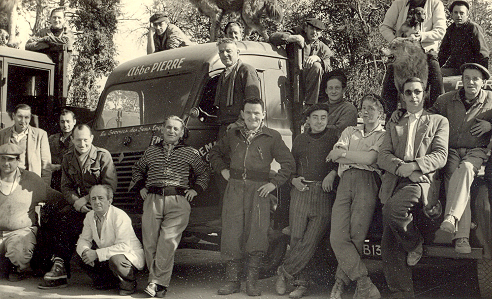 L'abbé Pierre au camp de la Pomponnette, devant la fourgonnette « Emmaüs, chiffonniers bâtisseurs », [1953]. © Emmaüs International